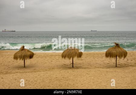 Drei Palmenschirme an einem leeren Strand in Valparaiso Chile an einem kalten Sommertag Stockfoto