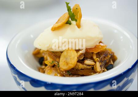 Nahaufnahme von karamellisierten Nüssen, getrockneten Früchten, einer Schaufel gefrorenen Vanillejoghurt auf einer kleinen Schüssel. Gesundes Café-Dessert. Leckeres Restaurant. Süßes Gericht. Stockfoto
