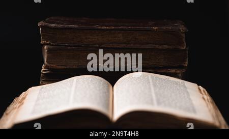 Offene verschwommene Torah-Seite und alte, abgenutzte jüdische Bücher mit Lederbindung im Hintergrund. Nahaufnahme. Selektiver Fokus Stockfoto