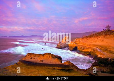 Die zerklüftete Küste mit Klippen und Felsformationen und die Brandung zieht sich bei Sonnenuntergang bis ans Ufer; Oregon, Vereinigte Staaten von Amerika Stockfoto