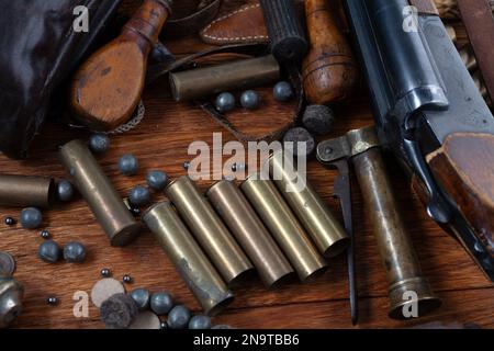 Antike 16-Gauge Break-Action glatt gebohrte Schrotflinte mit Messinggehäuse und Zubehör für Patronennachladung auf Holztisch. Stockfoto