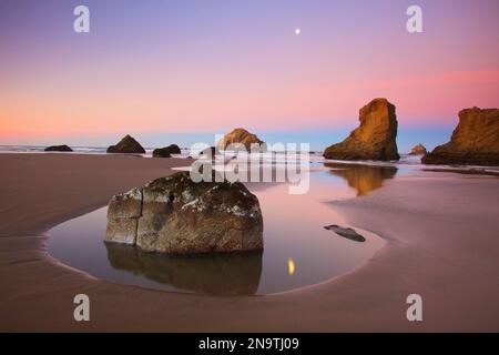 Monduntergang über Felsformationen, die sich bei Ebbe in Gezeitenbecken im Bandon State Natural Area an der Küste Oregons spiegeln Stockfoto