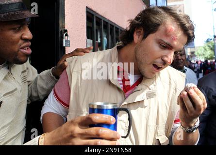 South Africa's M&G journalist Nickolaus Bauer is assisted by a shop owner after being hit by a stone during a protest by opposition party Democratic Alliance (DA) supporters against the Congress of South African Trade Unions (Cosatu) for opposing the youth wage subsidy in Johannesburg, South Africa on Tuesday May 15, 2012. An opposition party march in Johannesburg turned violent Tuesday after union supporters hurled rocks at the leader of South Africa's main opposition party. (AP Photo/Themba Hadebe)