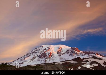 Schnee bedeckt den Felsen in einer Bergkette bei Sonnenaufgang mit warmem Sonnenlicht, das den Gipfel beleuchtet, vom Paradise Park in Mount Rainier Nation aus gesehen... Stockfoto