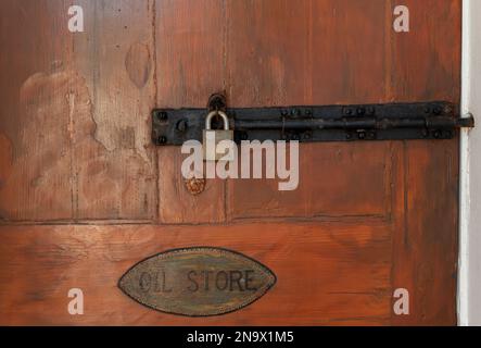 Vintage-Tür mit verschraubtem Verschluss, Messingschloss und Schild für Öllager. Stockfoto