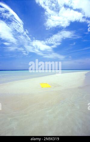 Hellgelbes Strandtuch auf einer kleinen weißen Sandbar, umgeben von klarem türkisfarbenem Meereswasser Stockfoto