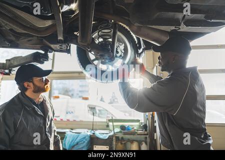 Zwei Mechaniker, die in der Autowerkstatt an einem Auto arbeiten, mittelgroß. Hochwertiges Foto Stockfoto