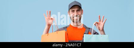 Happy Delivery Mann in Uniform hält Einkaufstaschen auf blauem Studiohintergrund Stockfoto