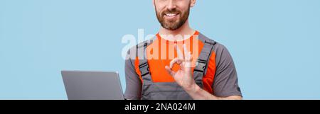 Gutaussehender lächelnder Mann in Uniform mit Laptop, der die Kamera ansah und ein Okey-Zeichen zeigte Stockfoto