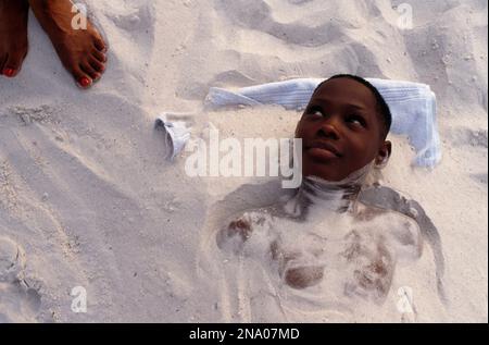 Der kleine Junge ist im weißen Sand an einem Strand begraben, während er im Urlaub in Saint Petersburg Beach, Florida, ist Stockfoto