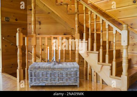 Gealterter taupe Korbkorb mit beleuchteten Kerzen vor der Kiefernholztreppe, die in den Keller und den oberen Stock vom Wohnzimmer in der Blockhütte führt. Stockfoto