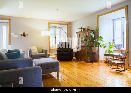 Grauer Polstersessel und Sofa plus brauner Ledersessel, antikes Holzbuffet, grüne Pflanzen- und Schaukelstuhl im Wohnzimmer des alten Hauses 1820. Stockfoto