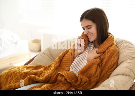 Eine Frau mit warmem orangefarbenem Karomuster, die zu Hause sitzt Stockfoto