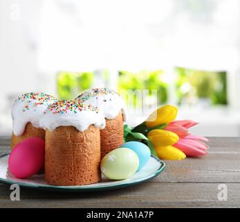 Köstliche Osterkuchen, bemalte Eier und Tulpen auf Holztisch im Haus Stockfoto