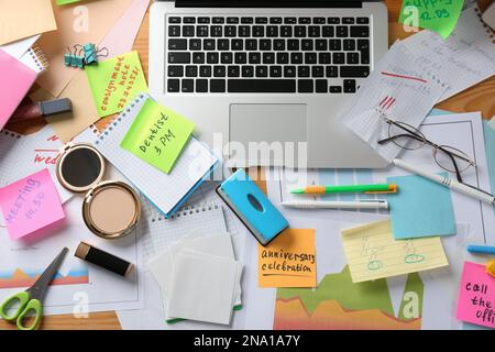 Unordentlicher Tisch mit Laptop und Kosmetik, flach liegend. Das Konzept, von der Arbeit überfordert zu werden Stockfoto