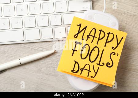 Computermaus mit Happy Fools' Day Note neben der Tastatur auf einem Holztisch, über der Sicht Stockfoto