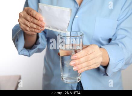 Frau, die Pulver aus dem Arzneimittelbeutel mit Wasser in das Glas gießt, Nahaufnahme Stockfoto