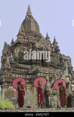 Mönche mit Regenschirmen stehen vor den Ruinen eines buddhistischen Tempels; Bagan, Myanmar Stockfoto