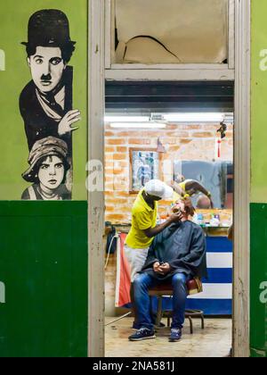 Friseur mit einem Mann, der sich rasiert, und ein Bild von Charlie Chaplin an der Wand; Havanna, Kuba Stockfoto