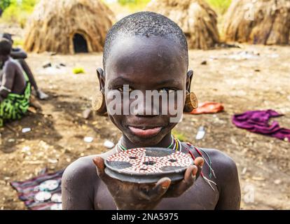 Mursi Boy zeigt eine Lippenplatte in einem Dorf im Mago National Park; Omo Valley, Äthiopien Stockfoto
