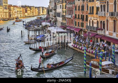 Gondeln und Gondoliere im Canale Grande mit Touristen entlang der bunten Uferpromenade; Venedig, Italien Stockfoto