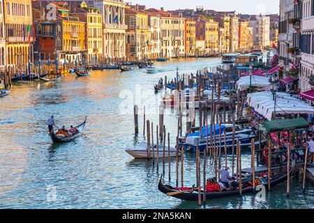 Gondeln und Gondoliere im Canale Grande mit Touristen entlang der bunten Uferpromenade; Venedig, Italien Stockfoto