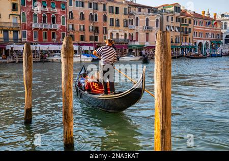 Gondeln und Gondoliere im Canale Grande mit Touristen entlang der bunten Uferpromenade; Venedig, Italien Stockfoto