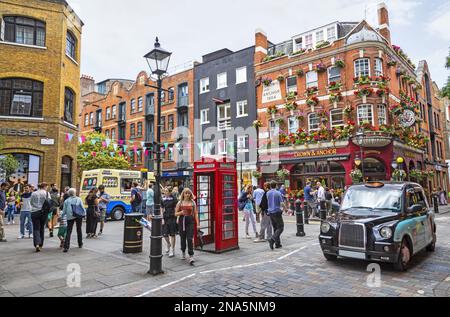 Geschäftige Straßenszene und Stadtleben an einer Straßenecke mit roter Telefonzelle; London, England Stockfoto