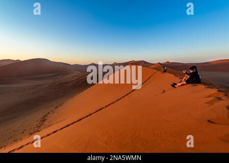 Touristen genießen den Sonnenaufgang von Dune 45, Sossusvlei, Namib Wüste; Namibia Stockfoto