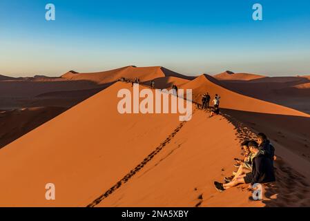 Touristen genießen den Sonnenaufgang von Dune 45, Sossusvlei, Namib Wüste; Namibia Stockfoto