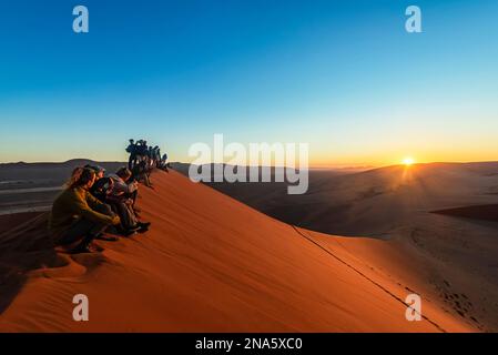 Touristen genießen den Sonnenaufgang von Dune 45, Sossusvlei, Namib Wüste; Namibia Stockfoto