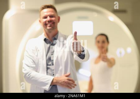 Männlicher Radiologe und weibliche Patientin mit Daumen nach oben in der Nähe des CT-Scanners im Krankenhaus. Stockfoto