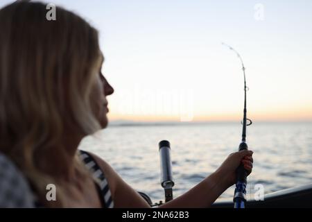 Eine Fischerin hält eine rotierende Angel in der Hand und schaut auf das Meer, während sie vom Boot aus angeln. Stockfoto