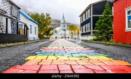 Der farbenfrohe Pfad lag mitten in einer Asphaltstraße, der zu einer weißen Kirche führte; Seydisfjordur, Eastern Region, Island Stockfoto