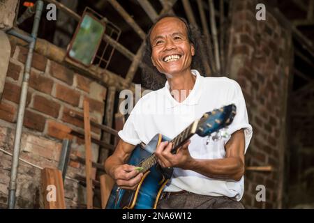 Eine Fahrradtour durch ein lokales vietnamesisches Dorf in Hoi an. Ein einheimischer Mann spielt Gitarre für die Touristen; Hoi an, Quang Nam, Vietnam Stockfoto