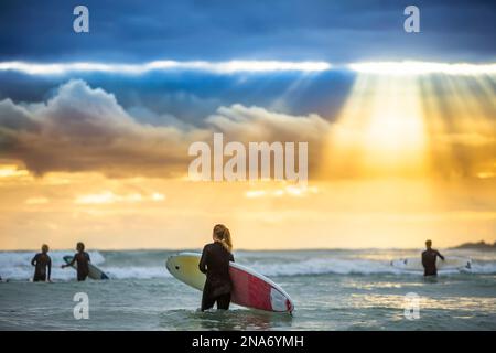 Ein wunderschöner Sonnenaufgang begrüßt die Surfer, die sich auf ein morgendliches Surfen vorbereiten und paddeln; Arrawarra, New South Wales, Australien Stockfoto