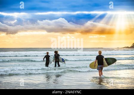 Ein wunderschöner Sonnenaufgang begrüßt die Surfer, die sich auf ein morgendliches Surfen vorbereiten und paddeln; Arrawarra, New South Wales, Australien Stockfoto