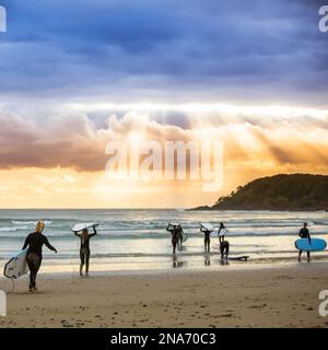 Ein wunderschöner Sonnenaufgang begrüßt die Surfer, die sich auf ein morgendliches Surfen vorbereiten und paddeln; Arrawarra, New South Wales, Australien Stockfoto