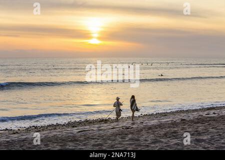 Surfer im Wasser und Menschen, die bei Sonnenuntergang am Strand spazieren gehen, San Onofre State Beach; San Clemente, Kalifornien, USA Stockfoto