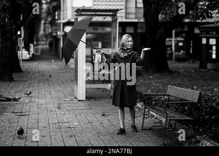 Eine Frau öffnet einen Schirm auf der Straße in der Stadt. Schwarzweißfoto. Stockfoto