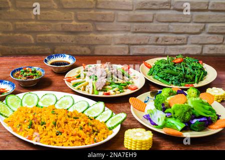 Vietnamesisches geschmortes Rindfleisch mit Papaya, gebratener Reis mit Schweinefleisch, Salat und Saucen auf einem Holztisch Stockfoto