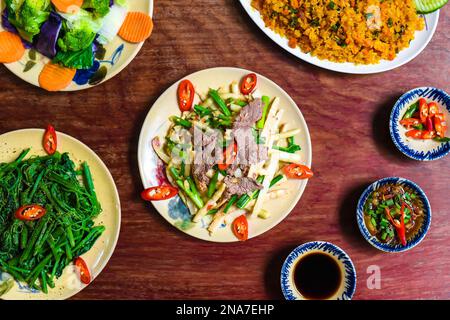 Vietnamesisches geschmortes Rindfleisch mit Papaya, gebratener Reis mit Schweinefleisch, Salat und Saucen auf einem Holztisch Stockfoto