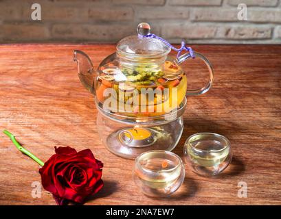 Kamillentee mit Goji-Beeren und Blumen mit Tassen und Rosenblüten auf einem Holztisch Stockfoto