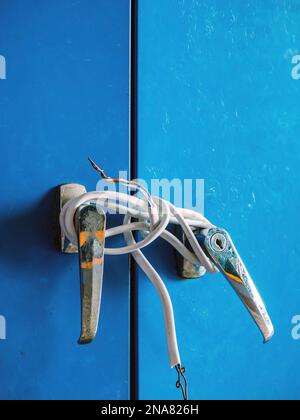 Bruchstücke weißer Elektrokabel wurden an silberne Knöpfe von Stahlschranktüren gebunden. Alte Tür mit Elektrokabel verriegelt. Blaues Schließfach mit o verriegelt Stockfoto