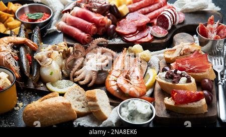 Typische spanische Tapas mit Jamonscheiben, Chorizo, Salami, Oliven, Kartoffelsnack Patatas bravas, Meeresfrüchte auf dunklem Tisch. Traditionelle spanische Küche. Stockfoto