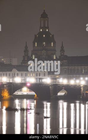 Dresden, Deutschland. 13. Februar 2023. Die Straßenbeleuchtung auf der Augustus-Brücke spiegelt sich morgens in der Elbe vor der Altstadt mit der Frauenkirche wider. Am 13. Februar erinnert die Hauptstadt Dresden an die Zerstörung der Stadt während des Zweiten Weltkriegs vor 78 Jahren. Am 13. Und 14. Februar 1945 reduzierten die alliierten Bomber das Zentrum der Stadt auf der Elbe in Schutt und Asche. Bis zu 25.000 Menschen haben ihr Leben verloren. Kredit: Robert Michael/dpa/Alamy Live News Stockfoto