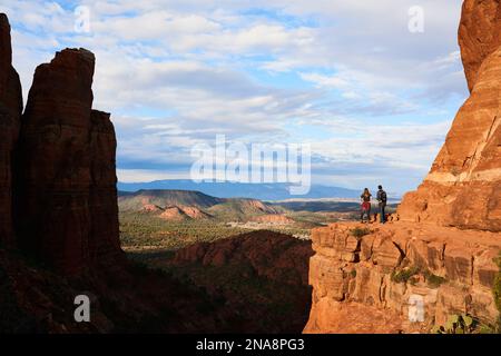 Zwei junge Wanderer stehen auf rotem Felsvorsprung und genießen einen atemberaubenden Blick auf den Sedona Canyon und die fernen Berge; Sedona, Arizona, Vereinigte Staaten von Amerika Stockfoto