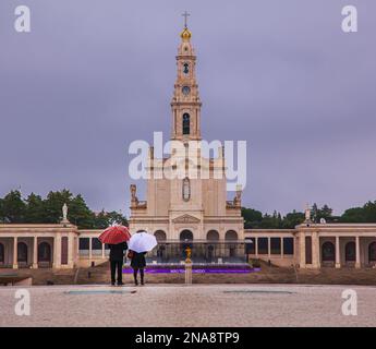 Touristen mit Sonnenschirmen, die auf die Basilika unserer Lieben Frau vom Rosenkranz, Heiligtum von Fatima, Fatima, Ourem, Portugal blicken Stockfoto