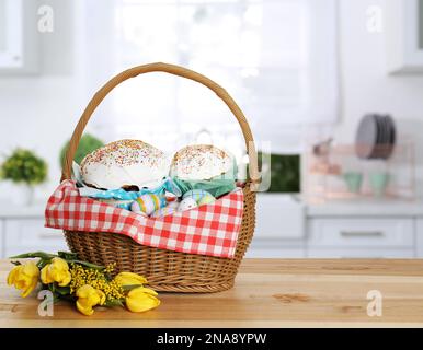 Korb mit köstlichen Osterkuchen, bemalten Eiern und Blumen auf Holztisch im Innenbereich. Platz für Text Stockfoto