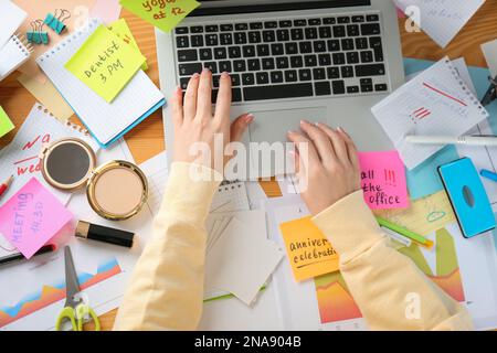 Frau, die ein Notebook am unordentlichen Tisch benutzt, Draufsicht. Das Konzept, von der Arbeit überfordert zu werden Stockfoto